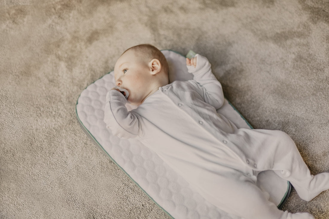 baby in white onesie lying on white and blue bed