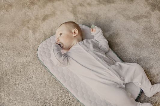 baby in white onesie lying on white and blue bed